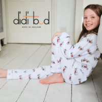 didi and bud, british made kids sleepwear, little girl in onesie sat on floor smiling next to her bed,